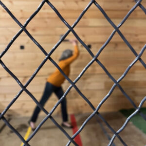 Gabrielle throwing an axe, as seen through metal fencing